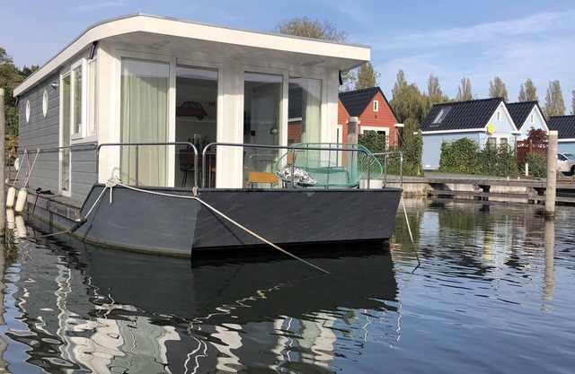 Modern houseboat in quiet harbor close to the IJsselmeer with SUPs and canoe
